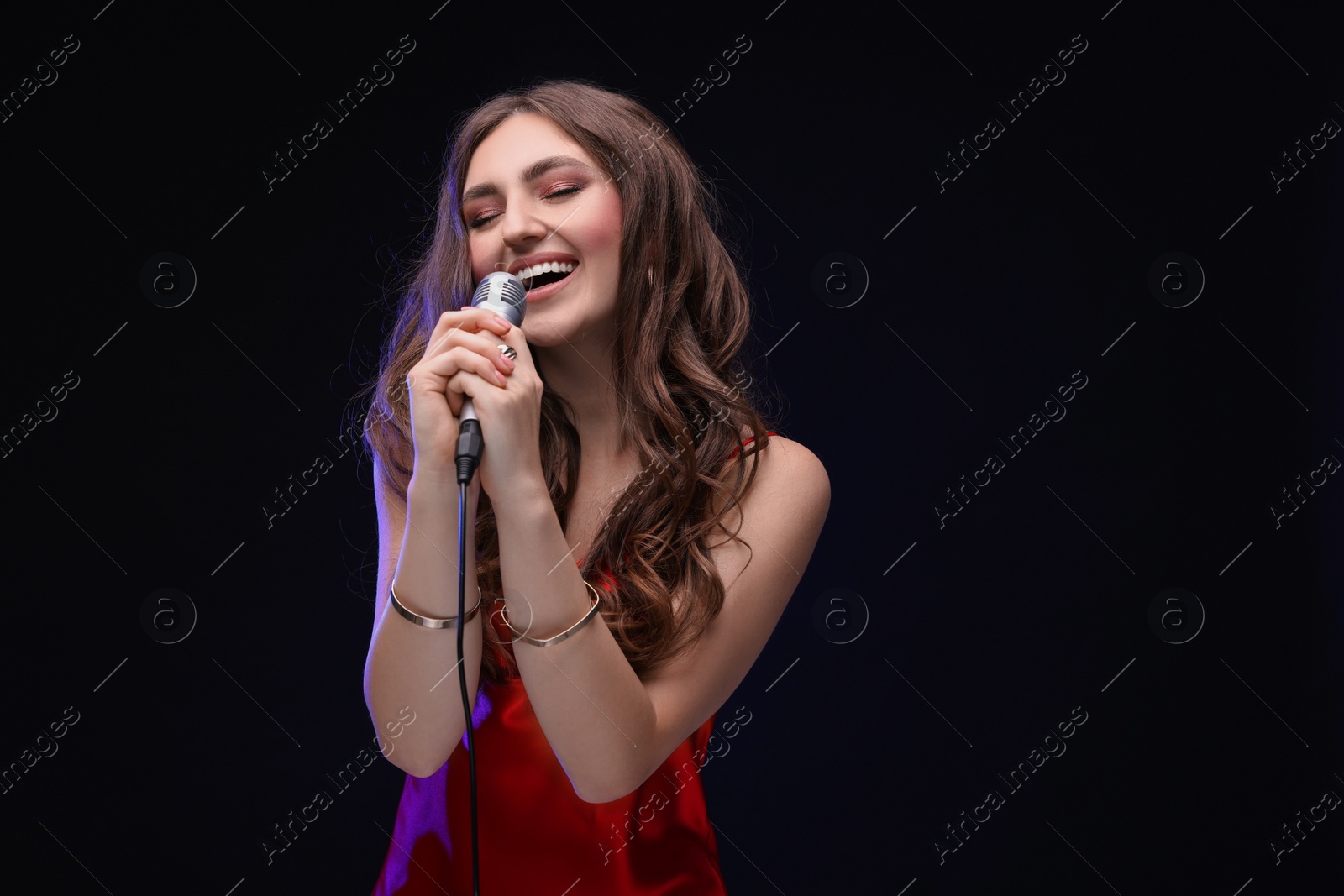 Photo of Emotional woman with microphone singing in color light on black background. Space for text