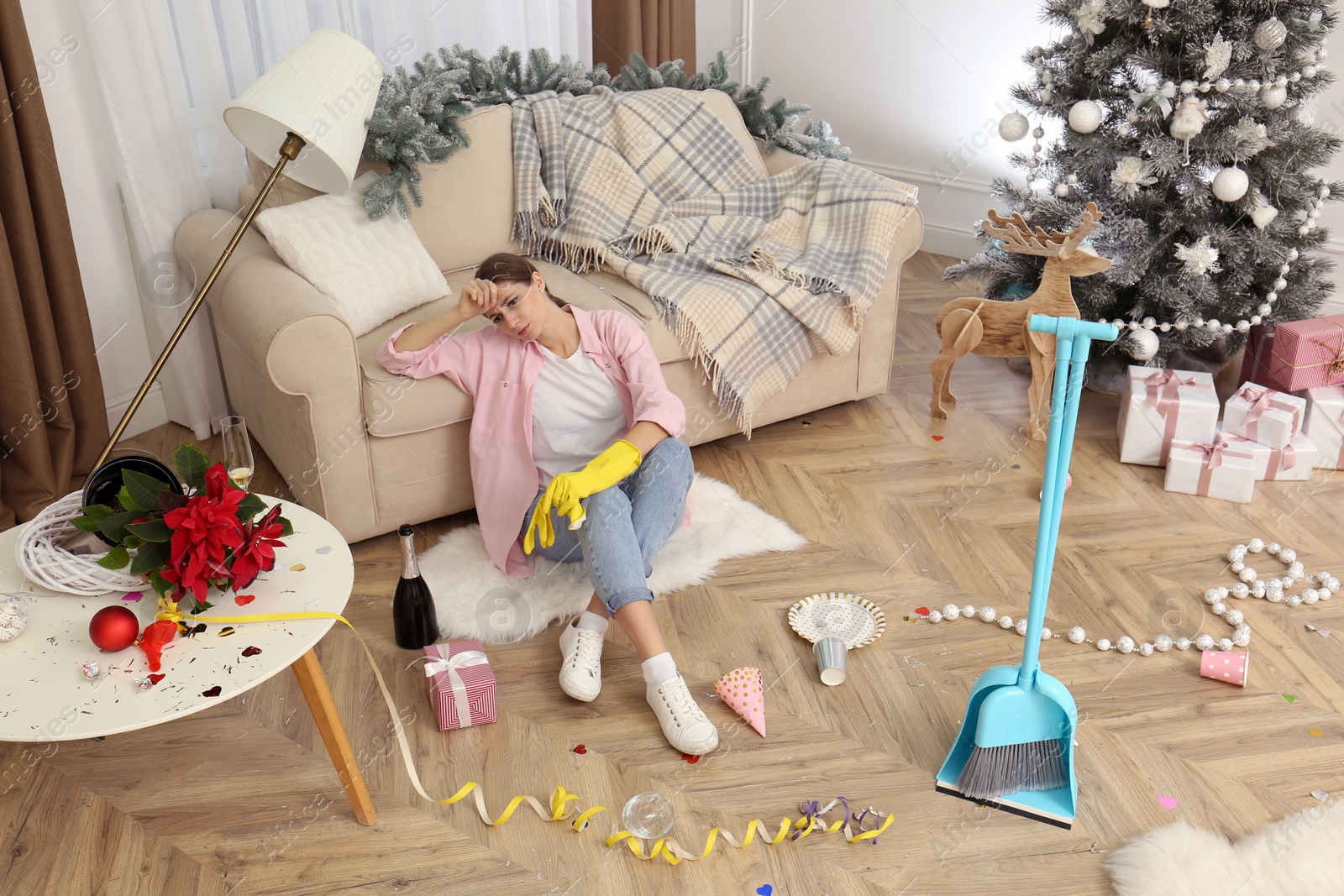 Photo of Tired woman sitting in messy room while cleaning after New Year party