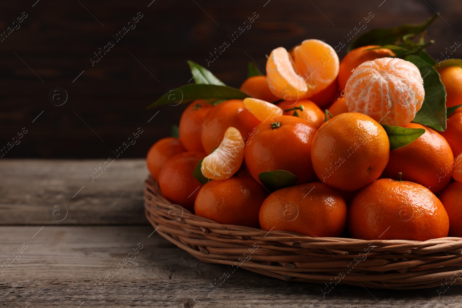 Photo of Fresh ripe juicy tangerines and green leaves on wooden table, space for text