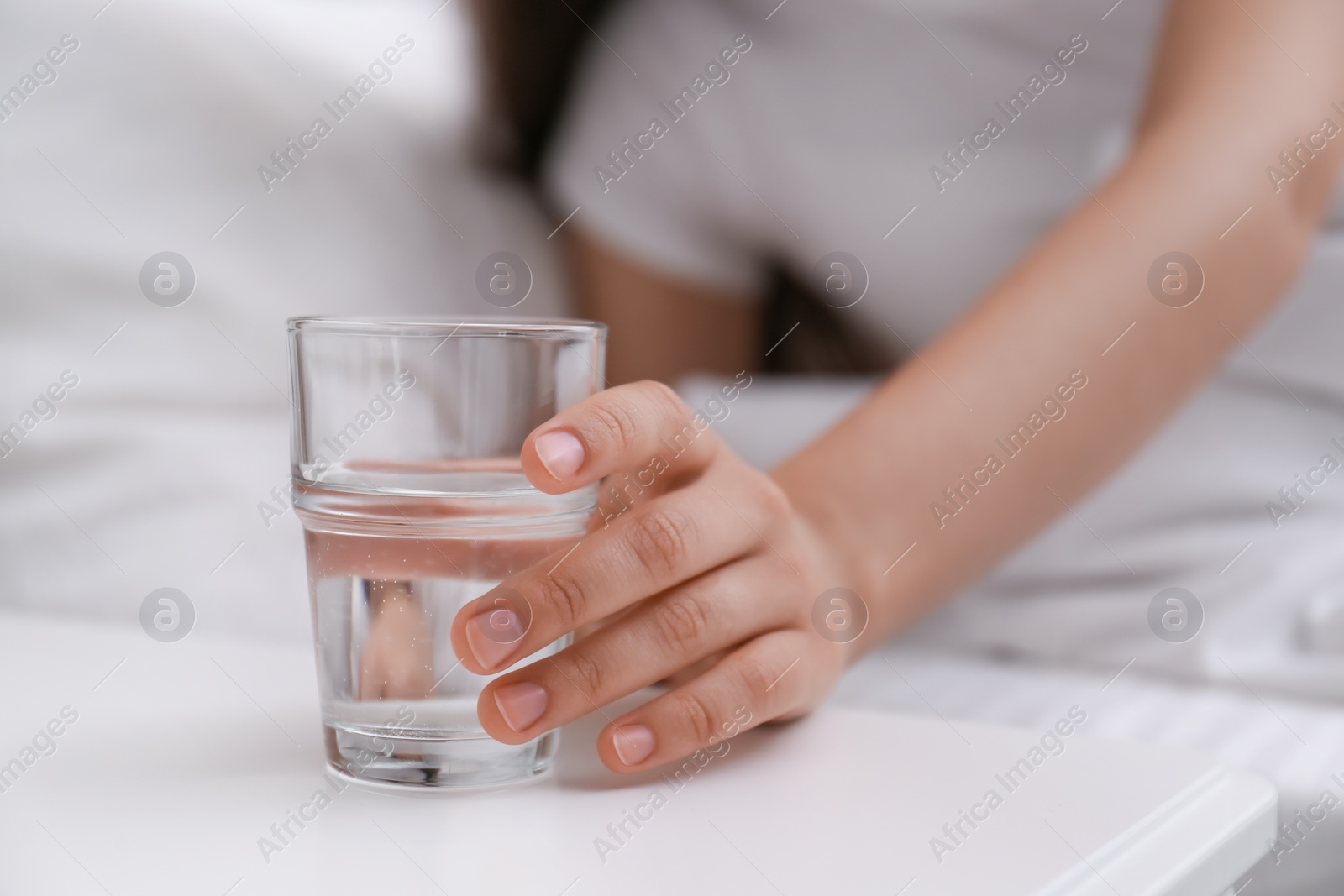 Photo of Young woman taking glass of water from nightstand at home, closeup
