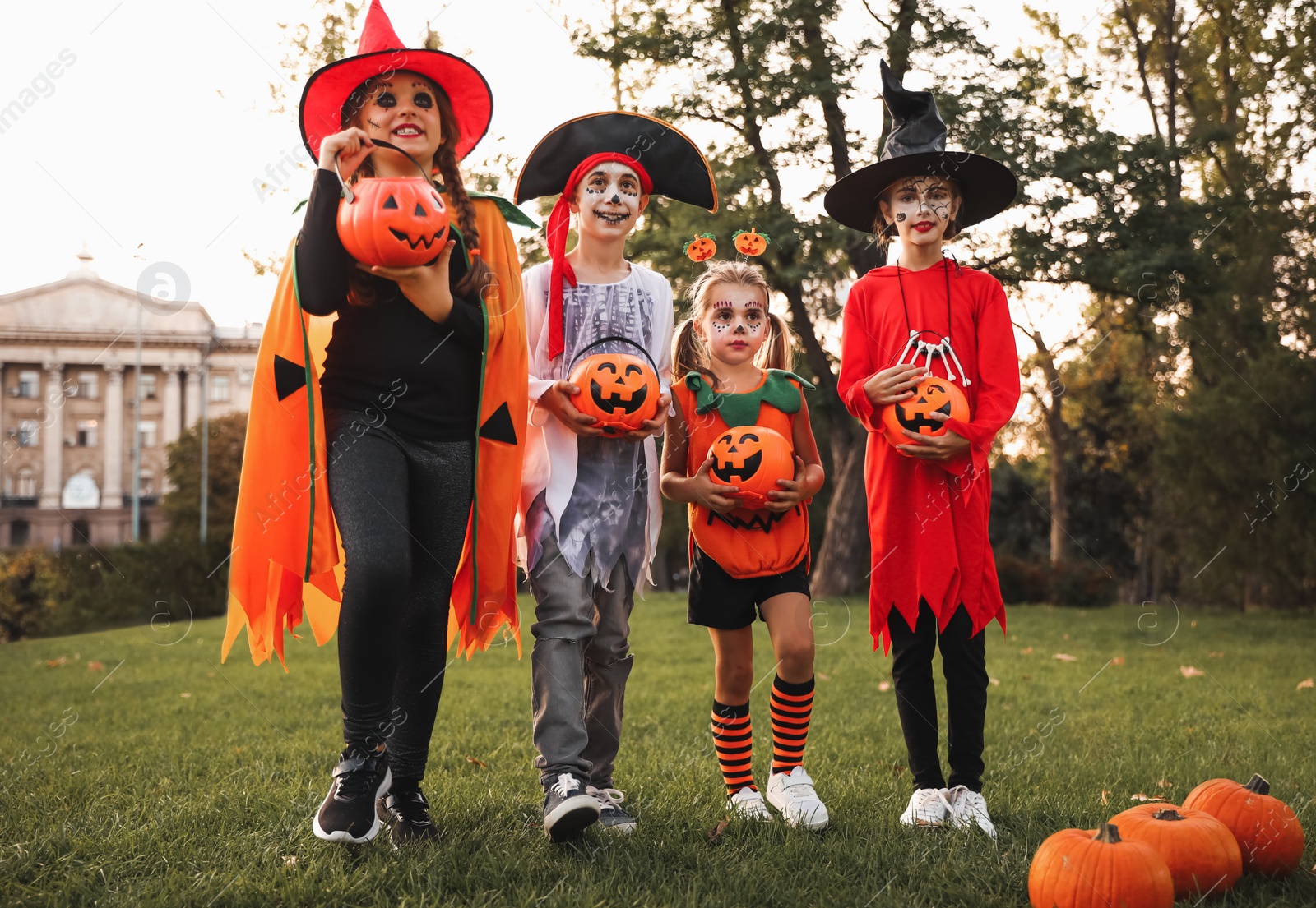 Photo of Cute little kids with pumpkin candy buckets wearing Halloween costumes in park