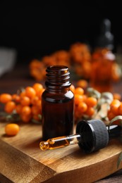 Photo of Ripe sea buckthorn and essential oil on wooden board against black background