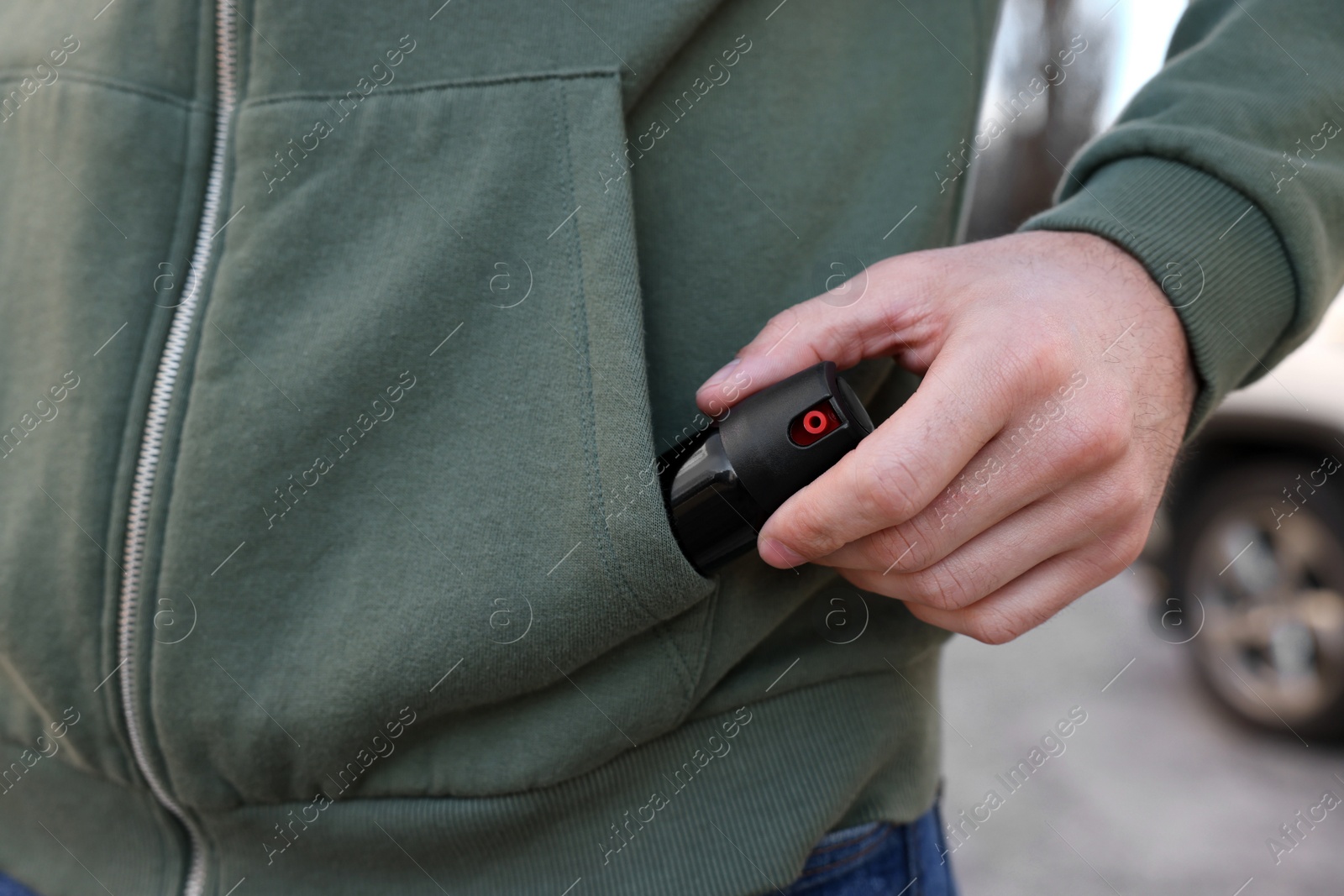Photo of Man putting pepper spray into sweater pocket outdoors, closeup
