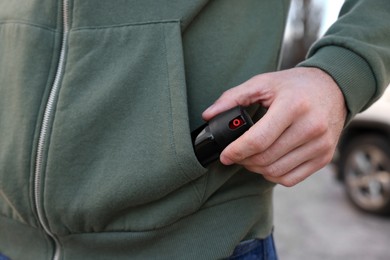 Man putting pepper spray into sweater pocket outdoors, closeup