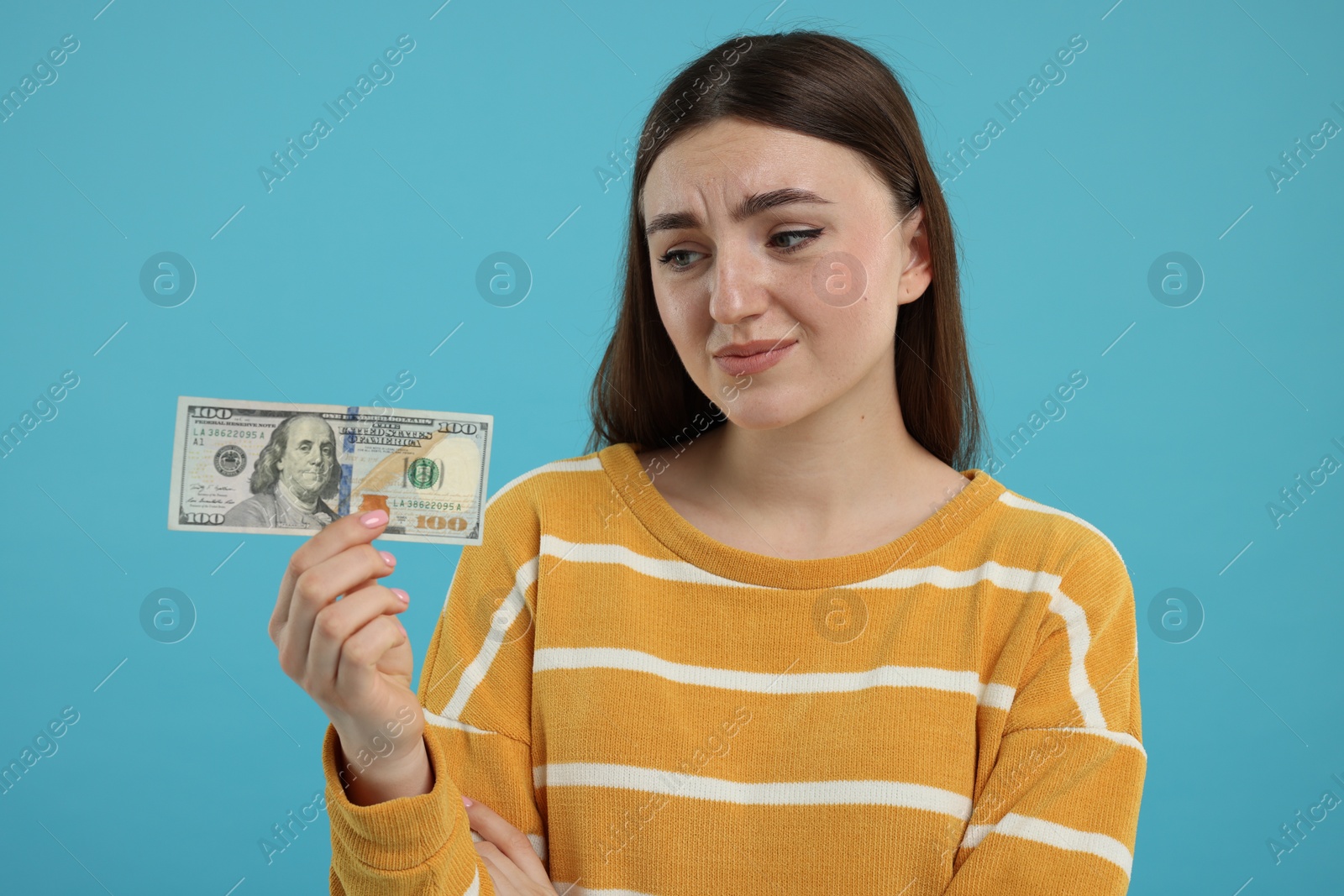 Photo of Sad woman with dollar banknote on light blue background