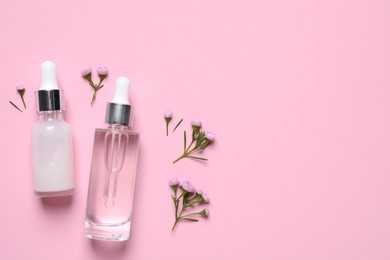 Bottles of cosmetic serums and beautiful flowers on pink background, flat lay. Space for text