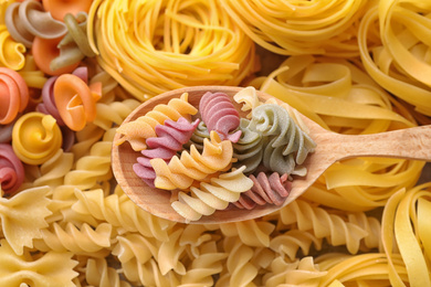 Wooden spoon and different types of pasta as background, top view