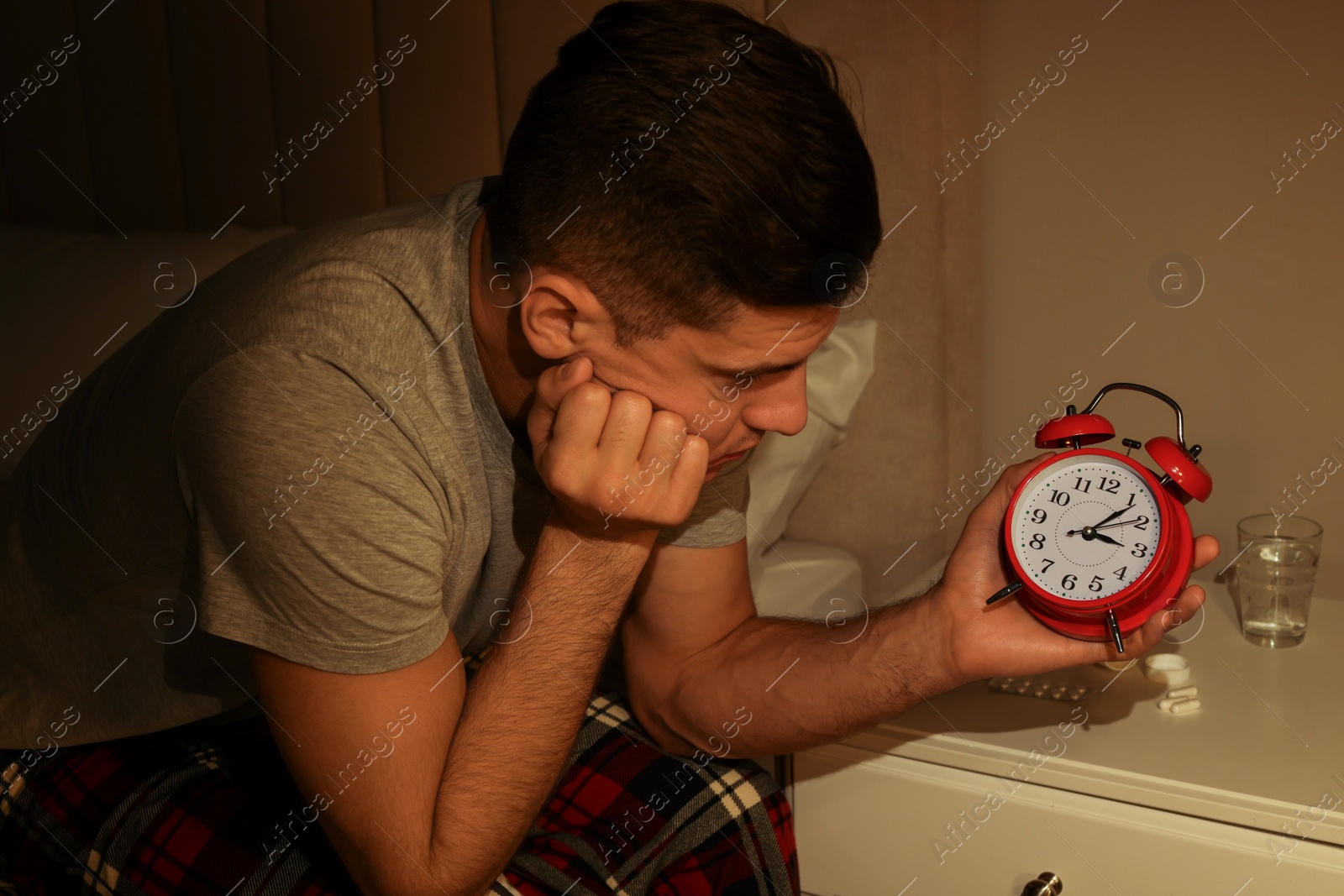 Photo of Man suffering from insomnia looking at time on alarm clock in bedroom
