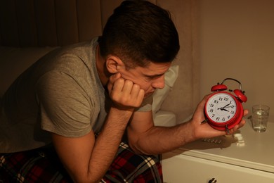 Photo of Man suffering from insomnia looking at time on alarm clock in bedroom