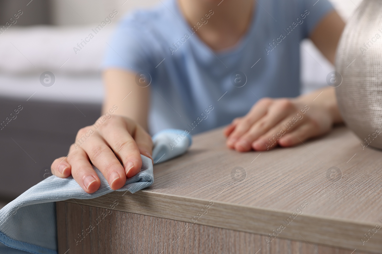 Photo of Woman with microfiber cloth cleaning wooden chest of drawers in room, closeup