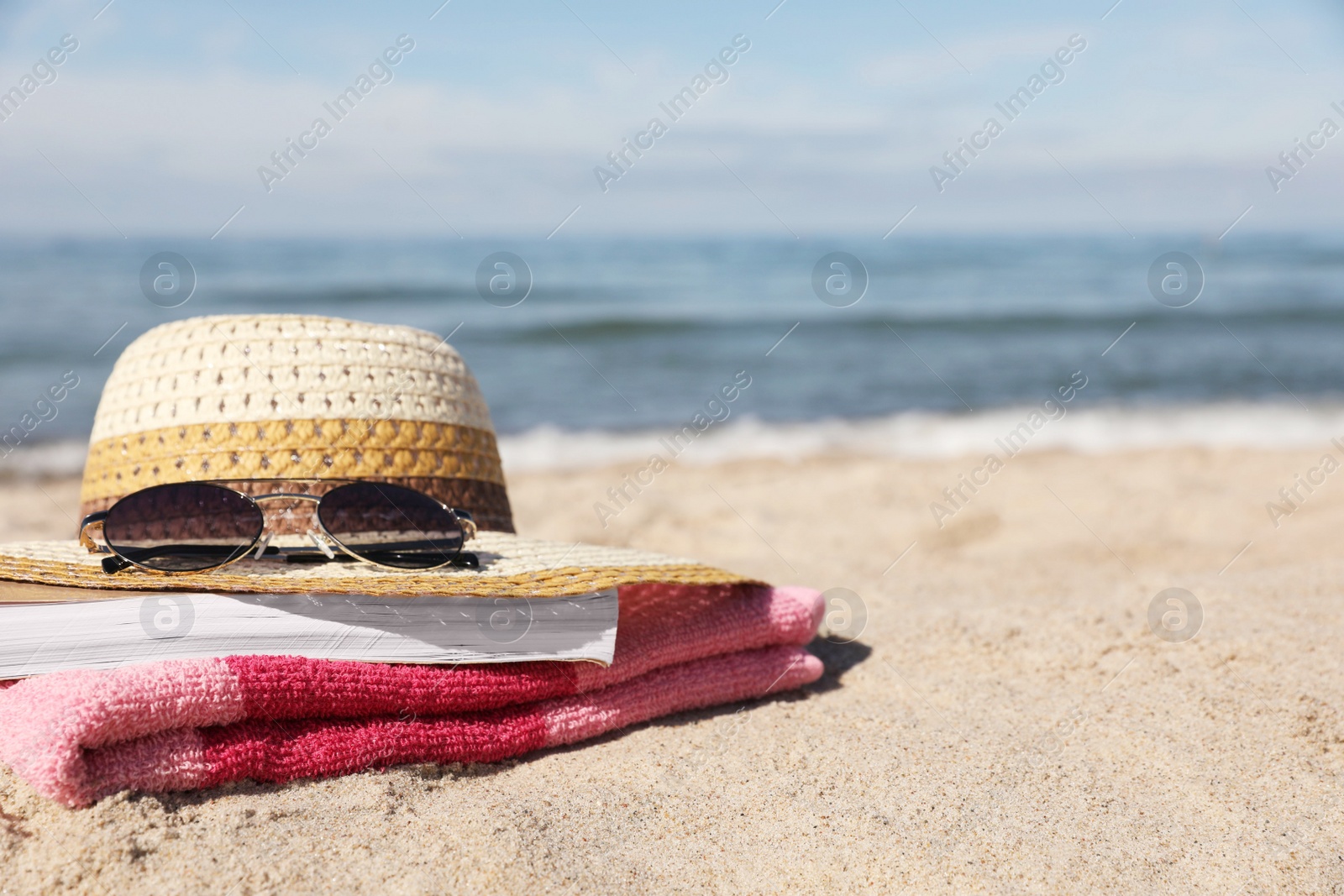 Photo of Hat, sunglasses, book and striped towel on sandy beach near sea, closeup. Space for text