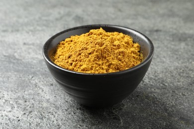 Photo of Dry curry powder in bowl on dark textured table, closeup
