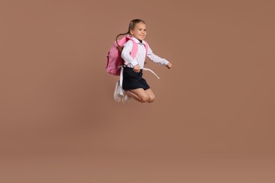 Happy schoolgirl with backpack jumping on brown background