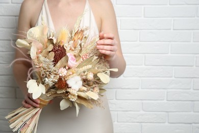 Bride holding beautiful dried flower bouquet near white brick wall, closeup. Space for text