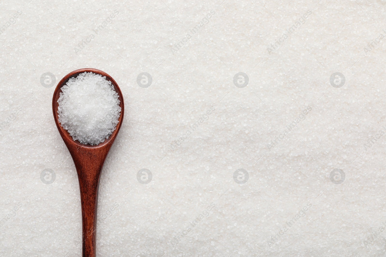 Photo of Wooden spoon on granulated sugar, top view. Space for text