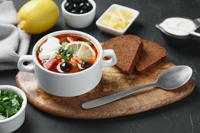 Photo of Meat solyanka soup with sausages, olives and vegetables in bowl served on dark grey textured table