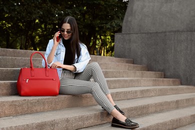 Young woman with stylish bag talking on phone outdoors, space for text