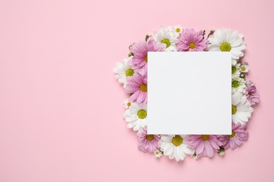 Photo of Beautiful chamomile flowers and paper card on pink background, flat lay with space for text