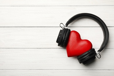 Photo of Decorative heart with modern headphones on wooden background, top view. Space for text