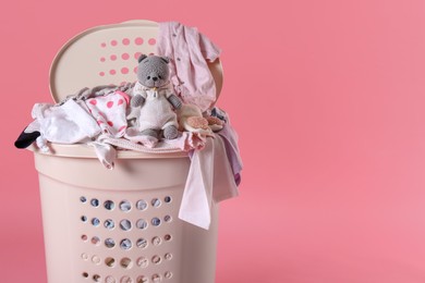 Laundry basket with baby clothes and soft toy on light pink background. Space for text