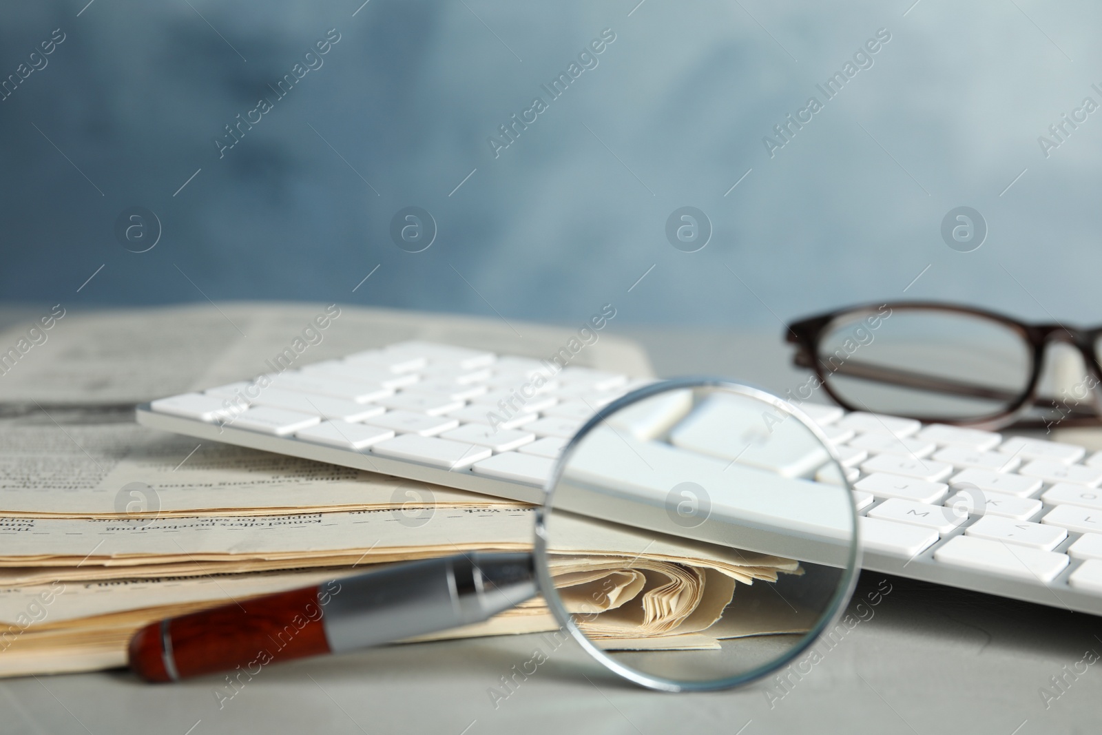 Photo of Magnifying glass, keyboard and stack of newspapers on grey table, space for text. Job search concept