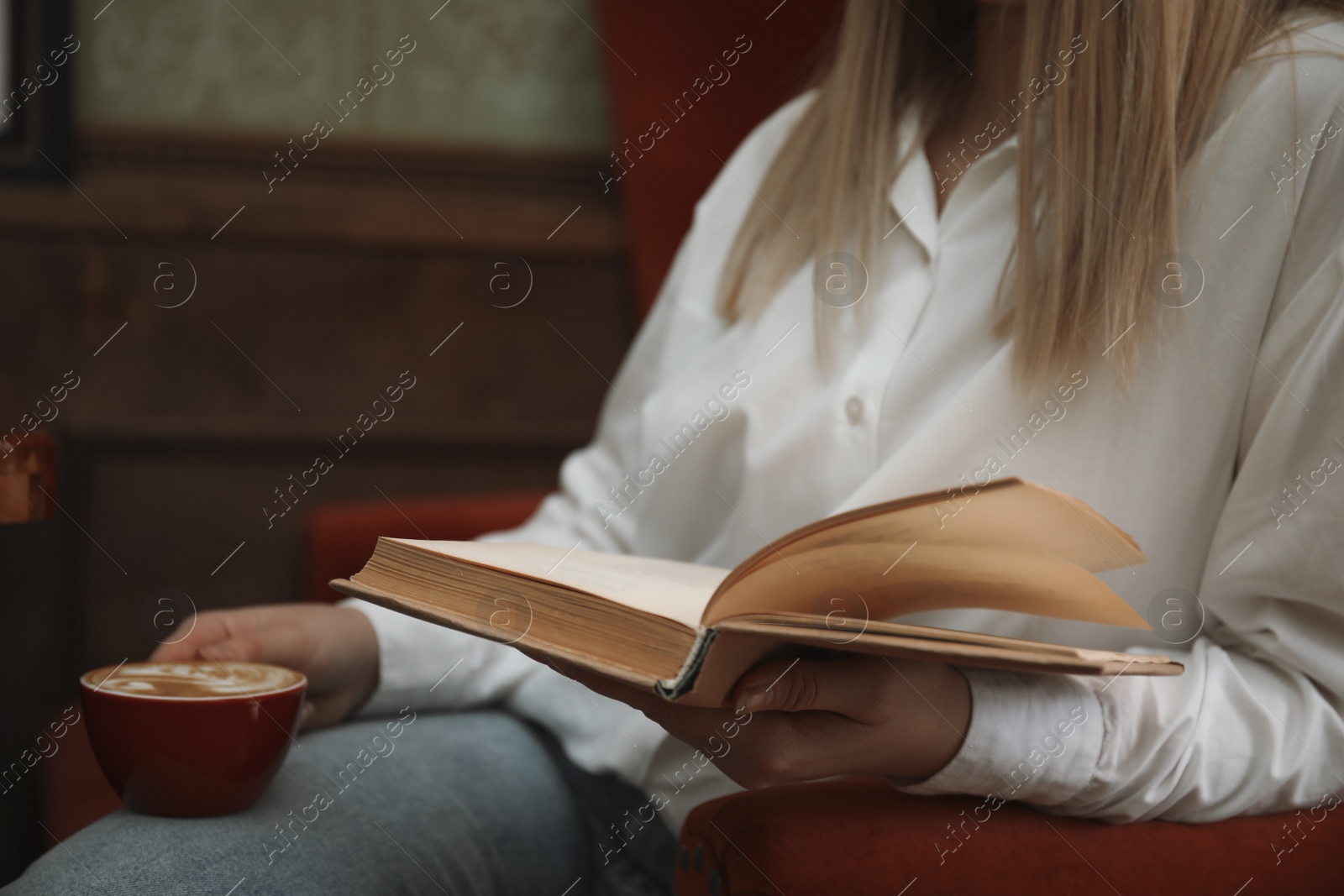 Photo of Woman with cup of coffee reading book indoors, closeup