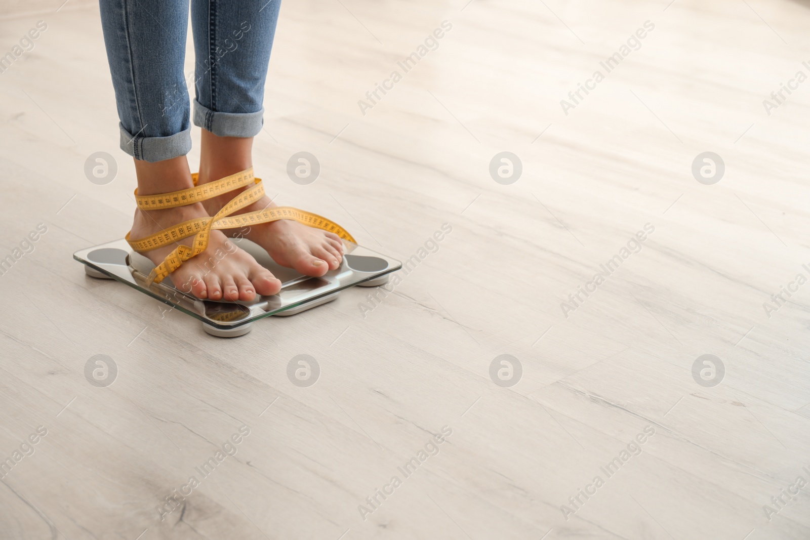 Photo of Woman with tape measuring her weight using scales on wooden floor. Healthy diet