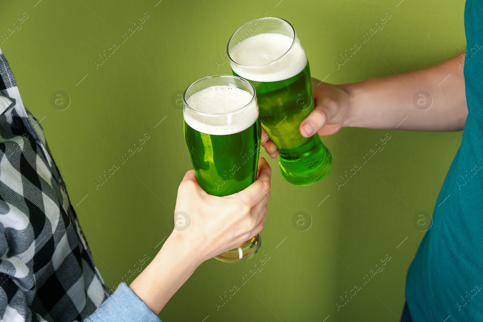 Photo of Man and woman toasting with green beer on color background, closeup. St. Patrick's Day celebration