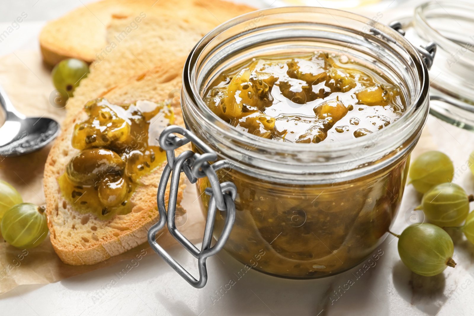 Photo of Jar with delicious gooseberry jam, fresh berries and toast on white table, closeup