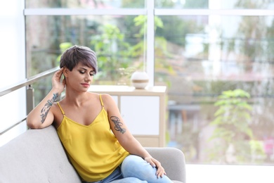 Trendy young woman with tattoos on sofa indoors