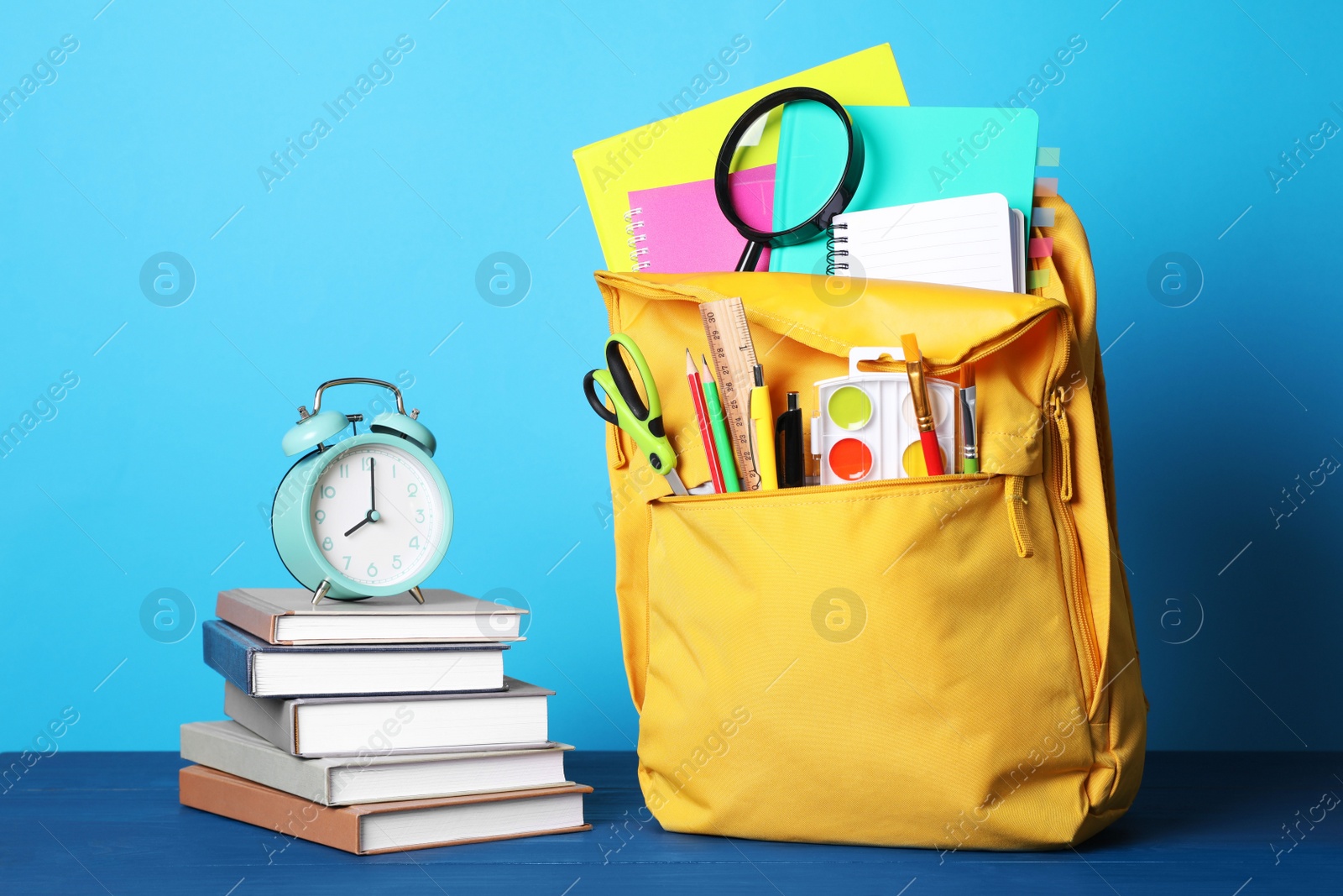 Photo of Yellow backpack and different school stationery on blue wooden table