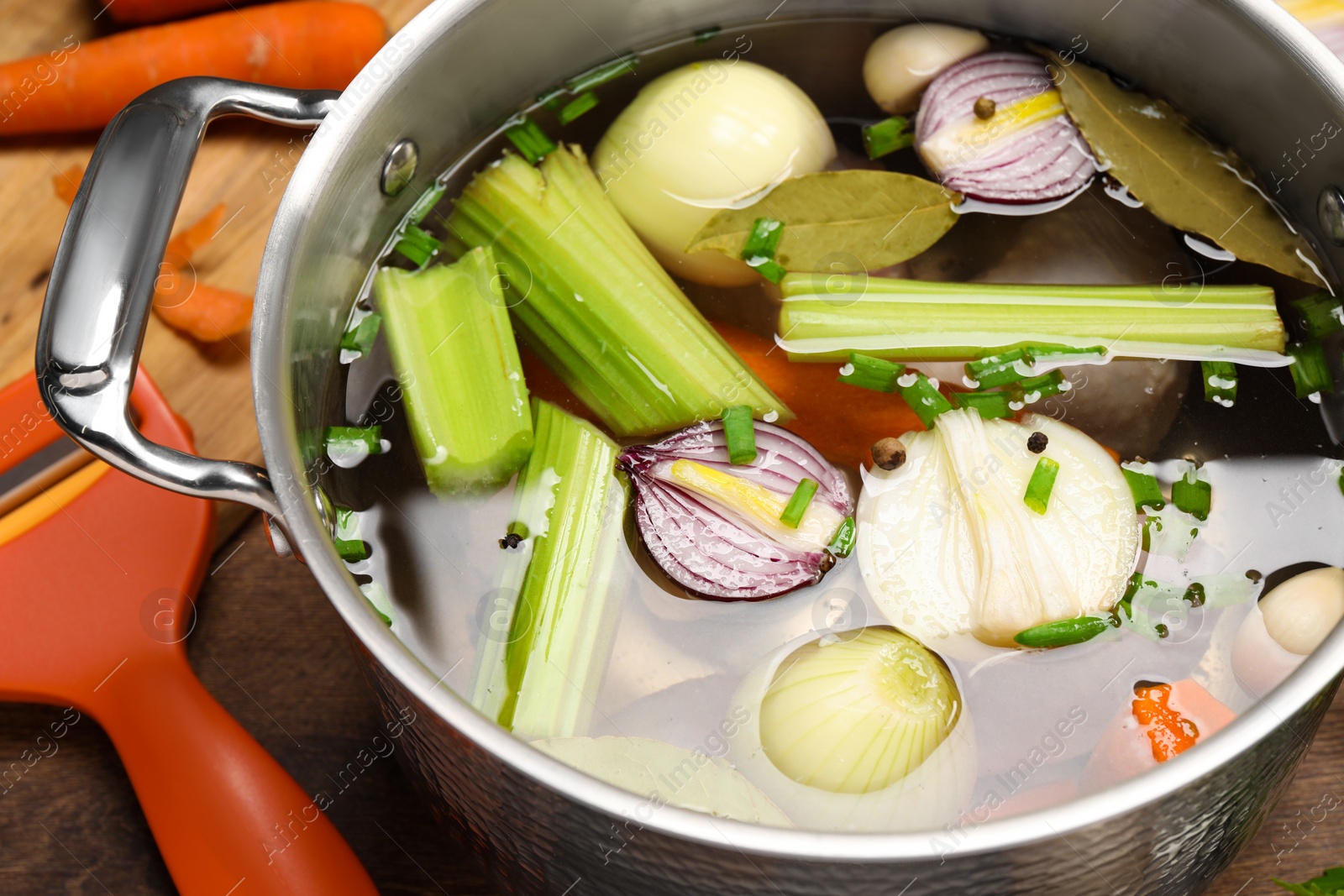 Photo of Pot with different ingredients for cooking tasty bouillon on wooden table, closeup