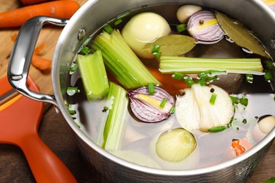 Pot with different ingredients for cooking tasty bouillon on wooden table, closeup