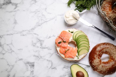 Photo of Delicious bagel with cream cheese, salmon and avocado on white marble table, flat lay. Space for text