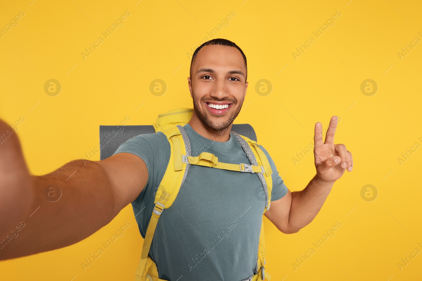 Photo of Happy tourist with backpack taking selfie on yellow background