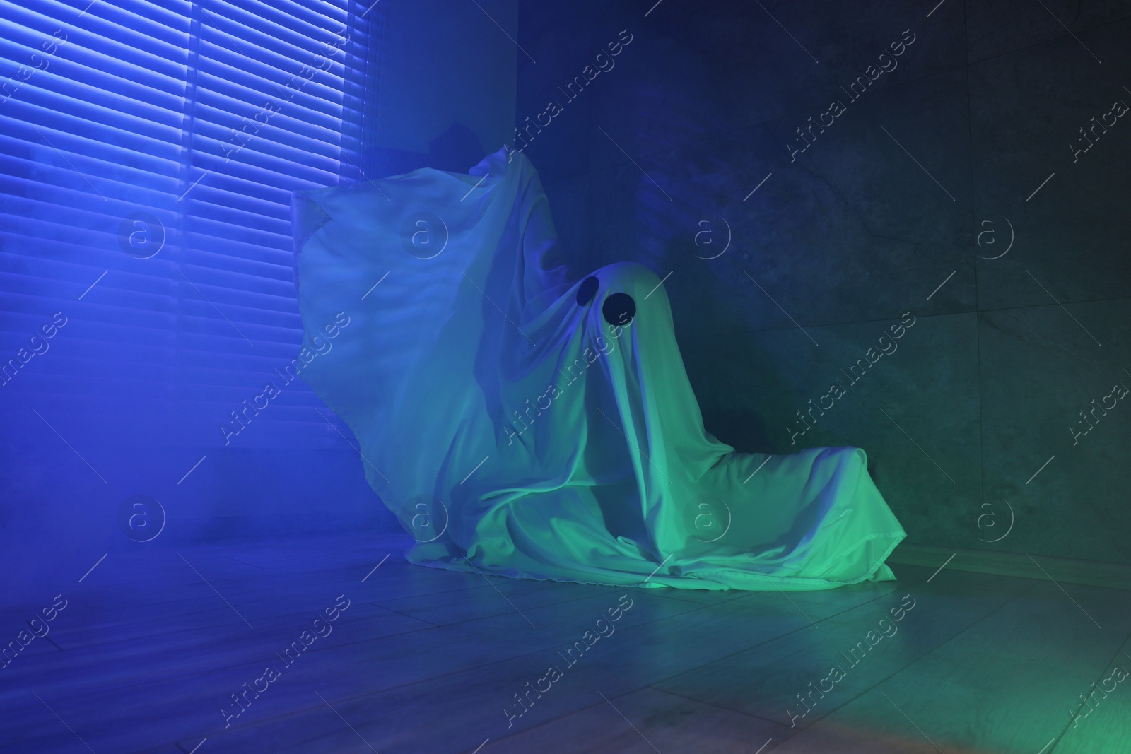 Photo of Creepy ghost. Woman covered with sheet near window in blue light