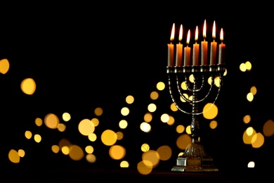 Photo of Golden menorah with burning candles against dark background and blurred festive lights, space for text