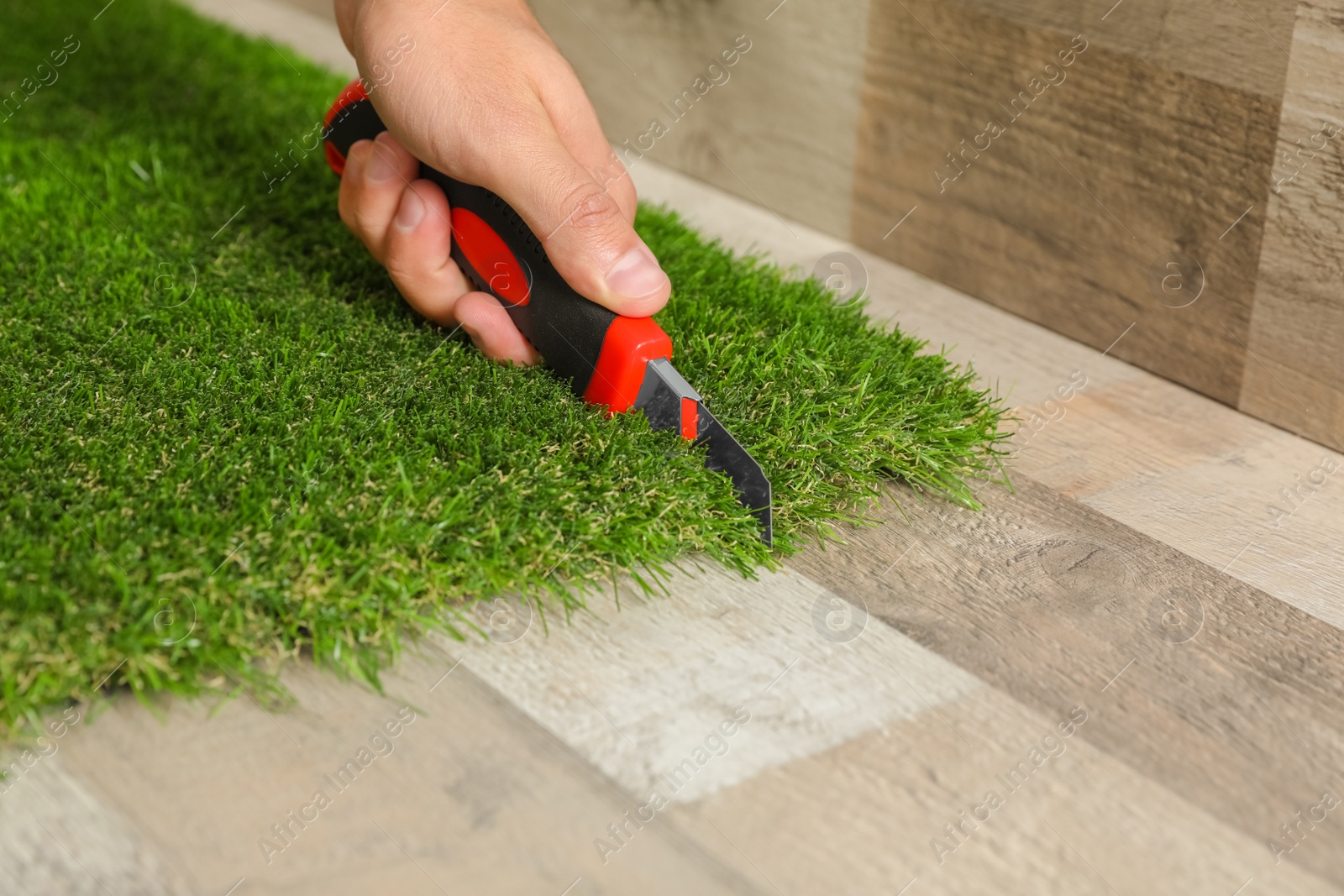 Photo of Man cutting artificial grass carpet indoors, closeup. Space for text