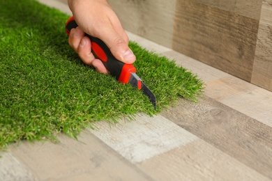 Man cutting artificial grass carpet indoors, closeup. Space for text