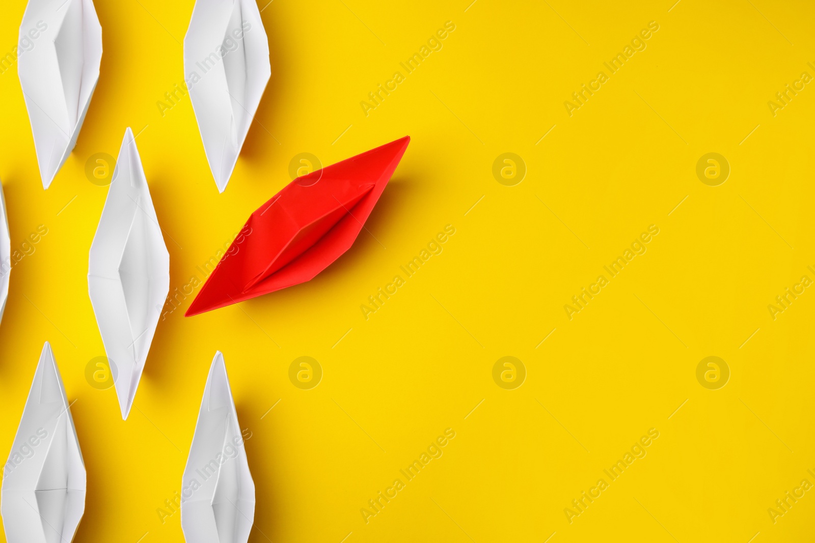 Photo of Red paper boat floating away from others on yellow background, flat lay with space for text. Uniqueness concept