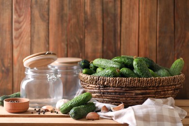 Photo of Fresh cucumbers and other ingredients near empty jars prepared for canning on wooden table