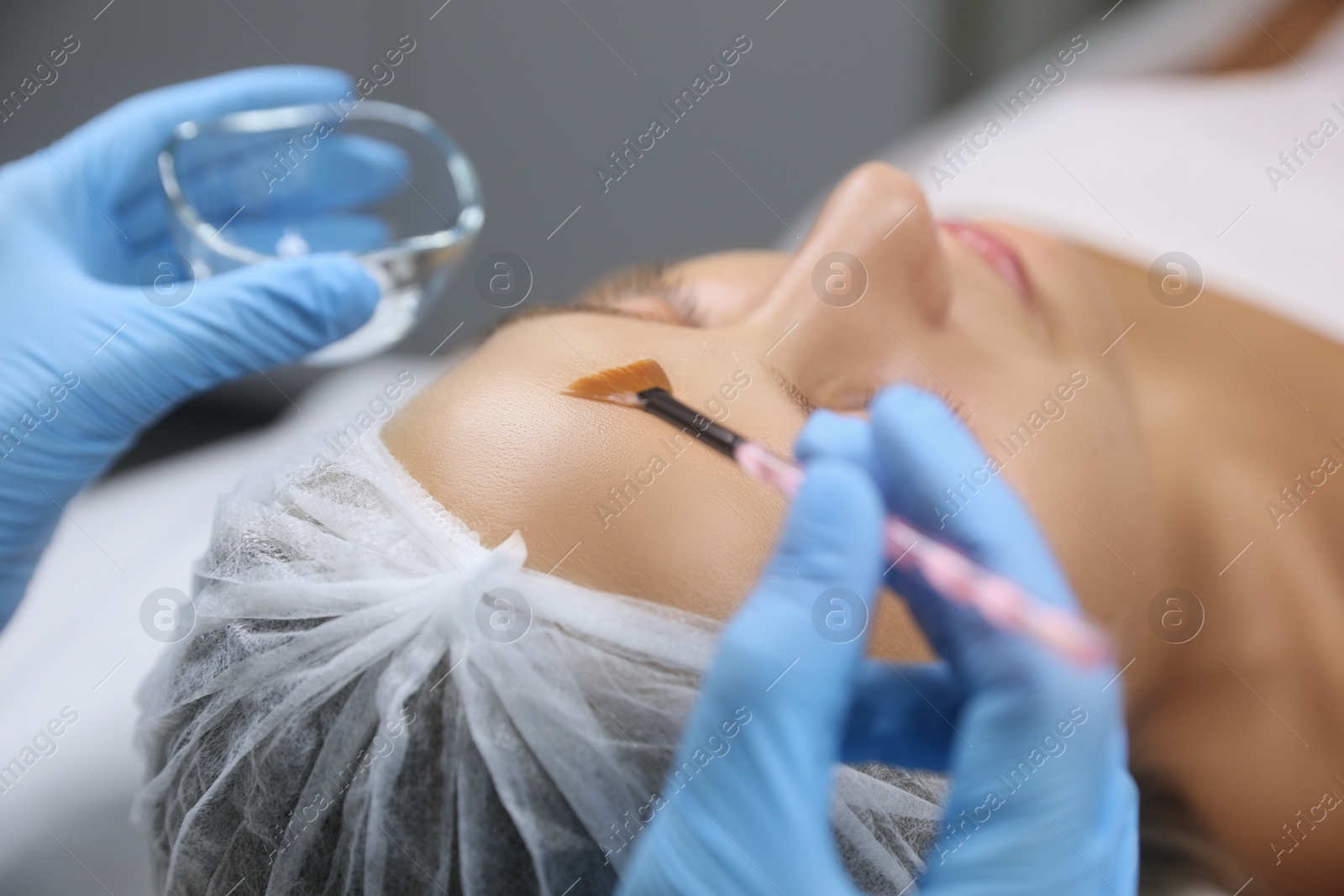 Photo of Cosmetologist applying chemical peel product on client's face in salon