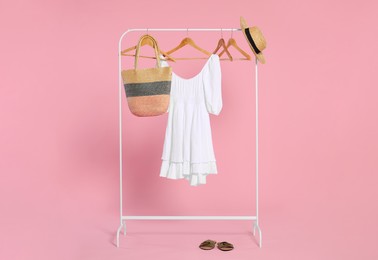 Photo of Rack with accessories and stylish white dress on wooden hangers against pink background