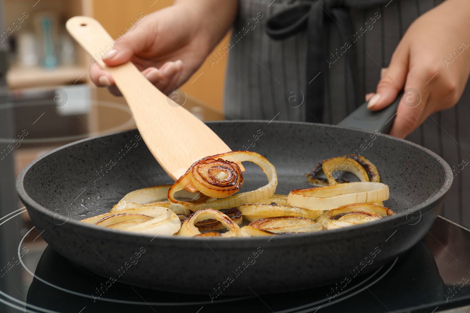 Photo of Woman cooking onion rings in frying pan on stove, closeup