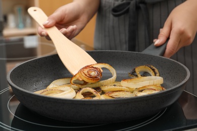 Photo of Woman cooking onion rings in frying pan on stove, closeup