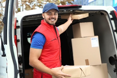 Photo of Young courier with parcels near delivery van outdoors