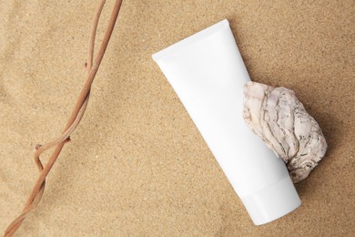 Photo of Tube with cream, shell and branches on sand, top view. Cosmetic product