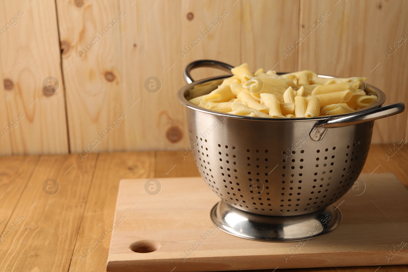Photo of Cooked pasta in metal colander on wooden table, closeup. Space for text