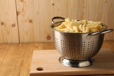 Cooked pasta in metal colander on wooden table, closeup. Space for text