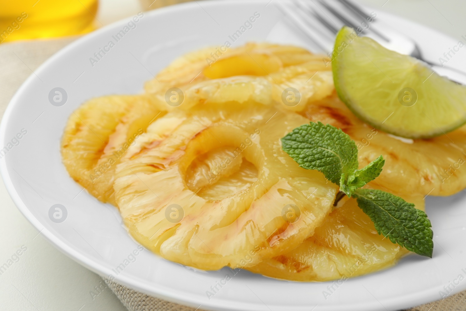 Photo of Tasty grilled pineapple slices, piece of lime and mint on white plate, closeup